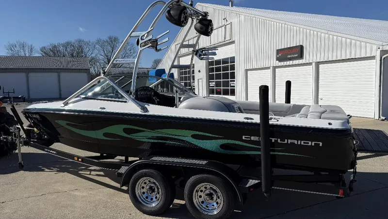 Slide: The Image of 2007 Centurion T5 boat with green flame design on trailer, parked outside a garage. - 5