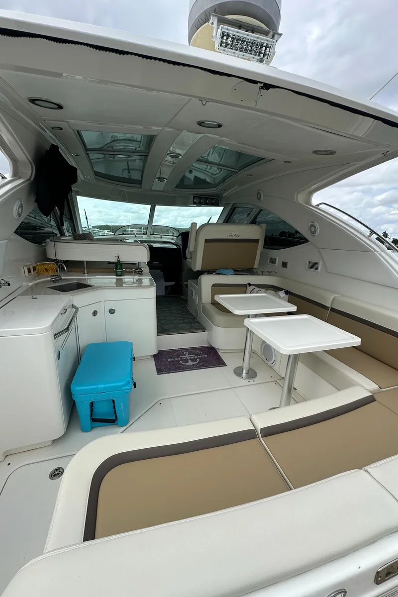 Slide: The Image of 2010 Sea Ray 470 Sundancer interior with seating, tables, and kitchenette under a cloudy sky. - 16