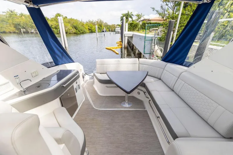 Slide: The Image of 2020 Sea Ray Sundancer 320 interior with elegant seating and table, docked by a scenic waterway. - 16