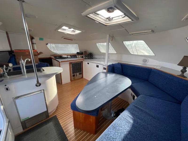 Slide: The Image of Interior of 2000 Manta 42 Catamaran with blue seating, dining table, and kitchenette. - 14