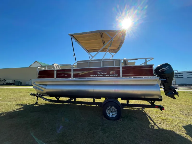 Slide: The Image of 2025 Sun Tracker Bass Buggy 18 DLX pontoon boat on trailer, sunny day. - 2