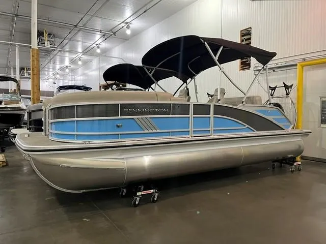 The Image of 2025 Bennington M22 Swingback pontoon boat in showroom, featuring blue accents and black canopy. - 0
