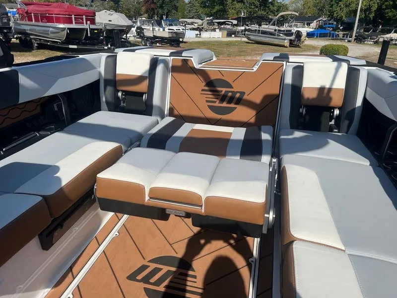 Slide: The Image of 2025 Malibu 23 LSV boat interior with brown and white seating, docked outdoors. - 11