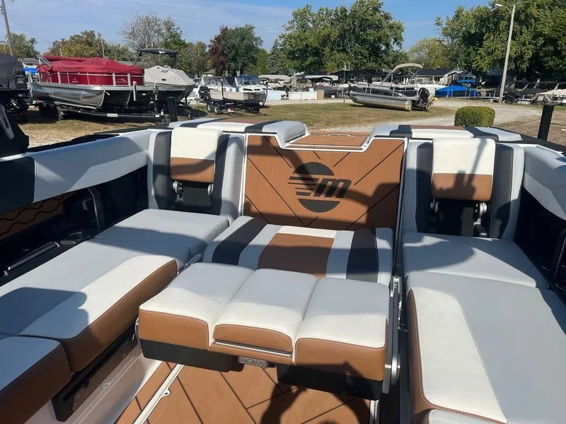 Slide: The Image of 2025 Malibu 23 LSV boat interior with brown and white seating, parked outdoors. - 12