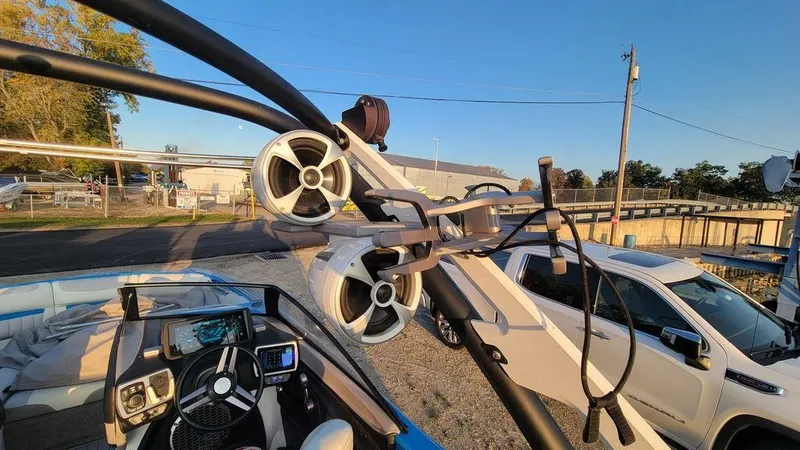 Slide: The Image of 2015 Malibu 24 MXZ boat with speakers and steering wheel, parked near a white vehicle. - 11