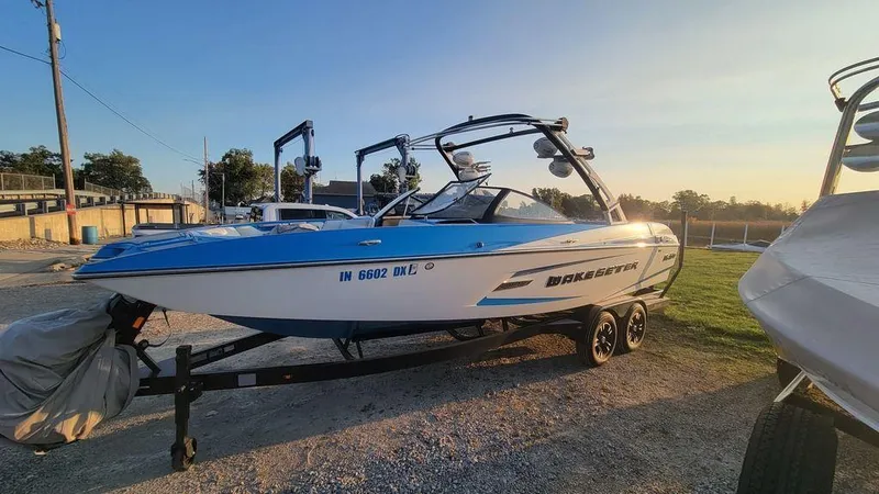 Slide: The Image of 2015 Malibu 24 MXZ boat on trailer, blue and white, parked outdoors at sunset. - 23