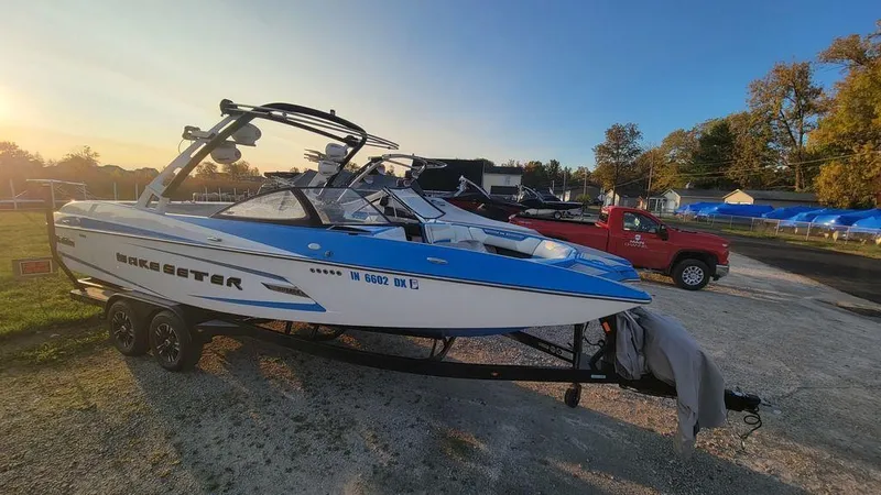 Slide: The Image of 2015 Malibu 24 MXZ boat on trailer, parked outdoors at sunset. - 24