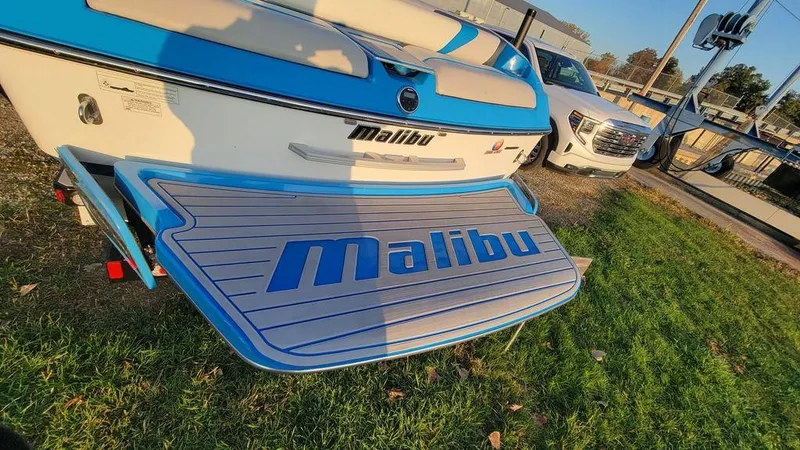 Slide: The Image of 2015 Malibu 24 MXZ boat with blue detailing on grass. - 27