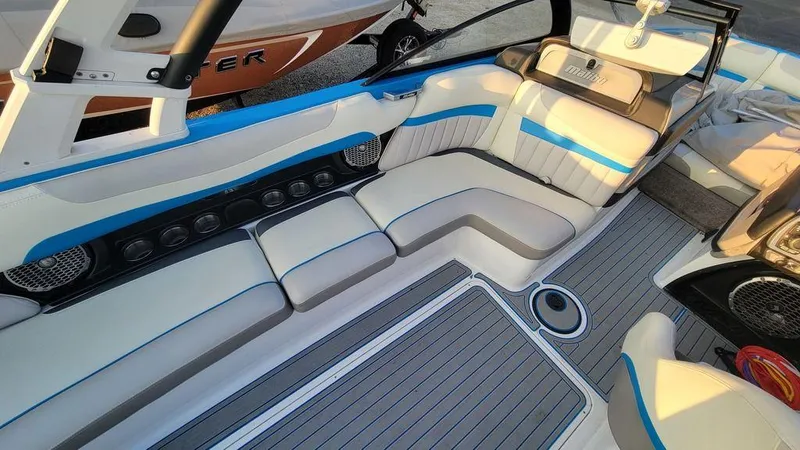 Slide: The Image of 2015 Malibu 24 MXZ boat interior with white and blue seating, gray flooring. - 8