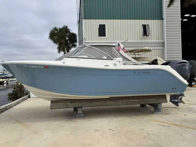 Slide: The Image of 2023 Cobia 220 DC boat in light blue, docked near a marina. - 1