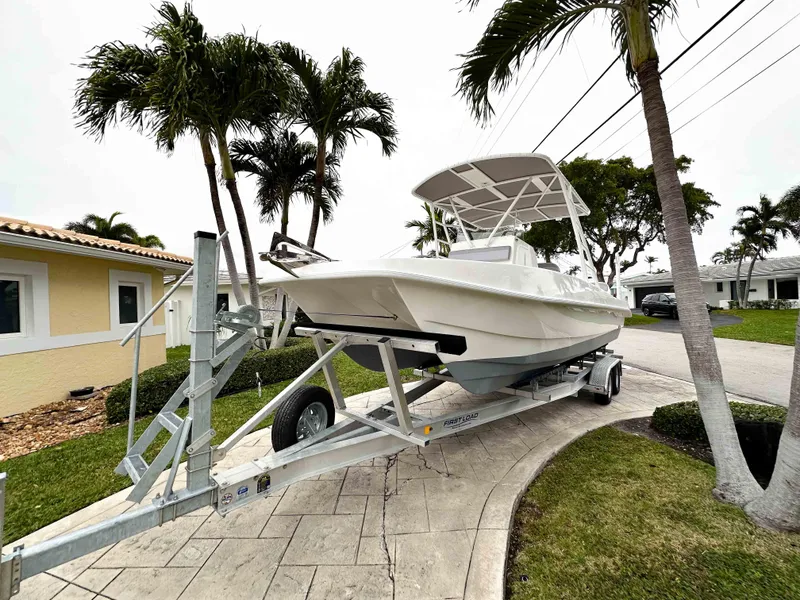 Slide: The Image of 2013 Twin Vee 26 Center Console boat on trailer, parked near palm trees. - 2