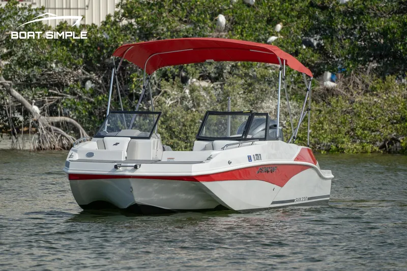Slide: The Image of 2024 Starcraft SVX 210 OB DC boat with red canopy on calm water. - 2