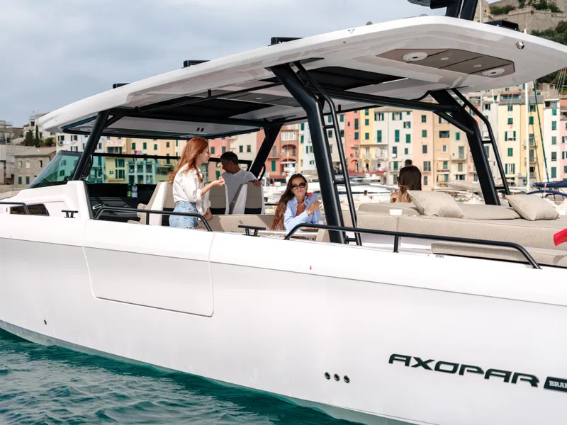 Slide: The Image of 2025 Axopar 45 SUN TOP boat with passengers, cruising near colorful waterfront buildings. - 10