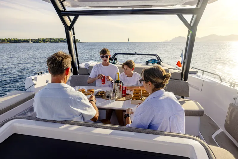 Slide: The Image of Family enjoying a meal on a 2025 Axopar 45 SUN TOP boat, surrounded by scenic ocean views. - 14