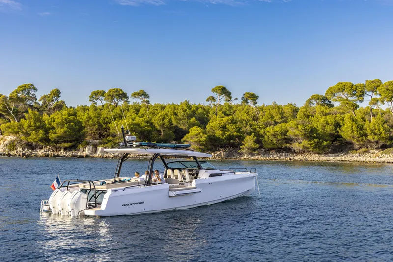 Slide: The Image of 2025 Axopar 45 SUN TOP boat cruising near a lush, tree-lined shoreline. - 4