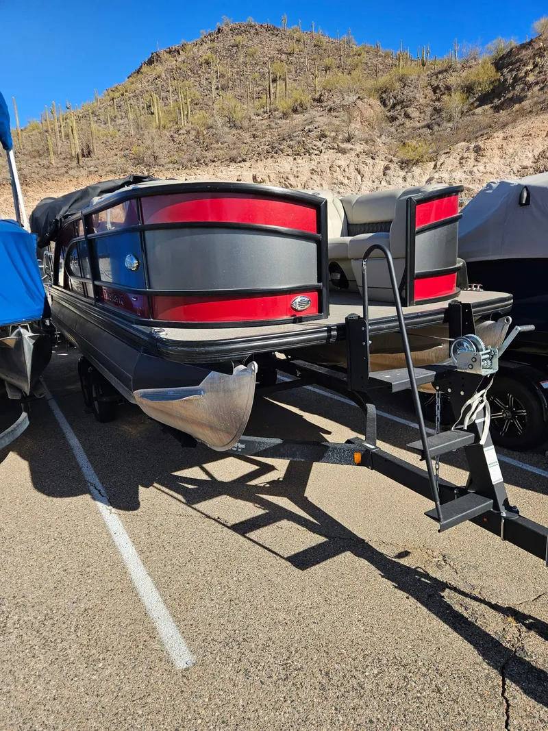 Slide: The Image of 2019 Barletta L21Q Pontoon boat on trailer, parked in a lot near a rocky hill. - 1
