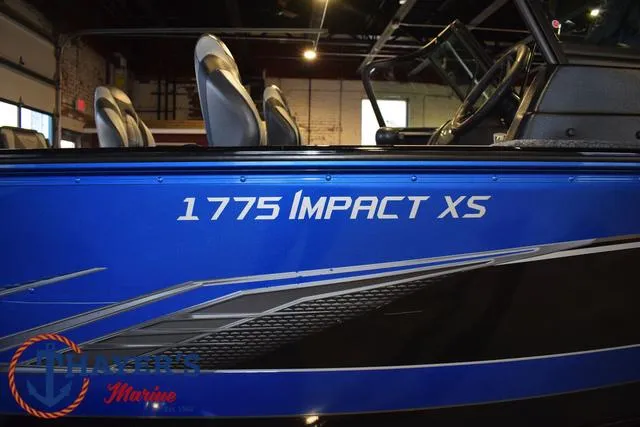 Slide: The Image of 2024 Lund 1775 Impact XS Sport boat, blue exterior with logo, displayed indoors. - 3
