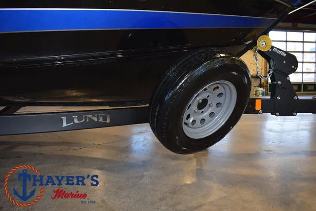 Slide: The Image of 2024 Lund 1775 Impact XS Sport boat trailer with visible wheel and Thayer's Marine logo. - 5