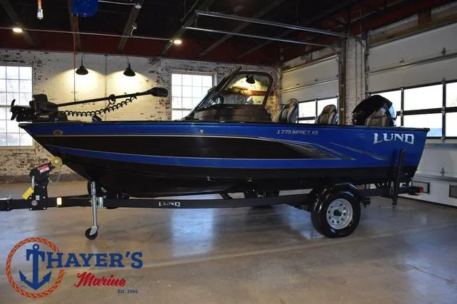 Slide: The Image of 2024 Lund 1775 Impact XS Sport boat in showroom, blue and black design, Thayer's Marine logo. - 7