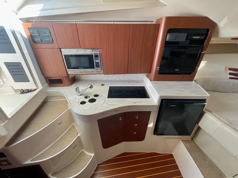Slide: The Image of 2015 Grady-White Express 330 interior kitchen with wood cabinets, stove, microwave, and compact fridge. - 31