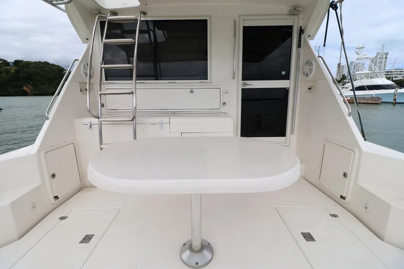 Slide: The Image of 2000 Riviera Flybridge Convertible yacht deck with table and ladder, docked by the water. - 22