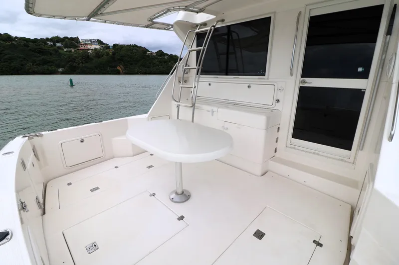 Slide: The Image of 2000 Riviera Flybridge Convertible yacht deck with table, ladder, and scenic water view. - 24