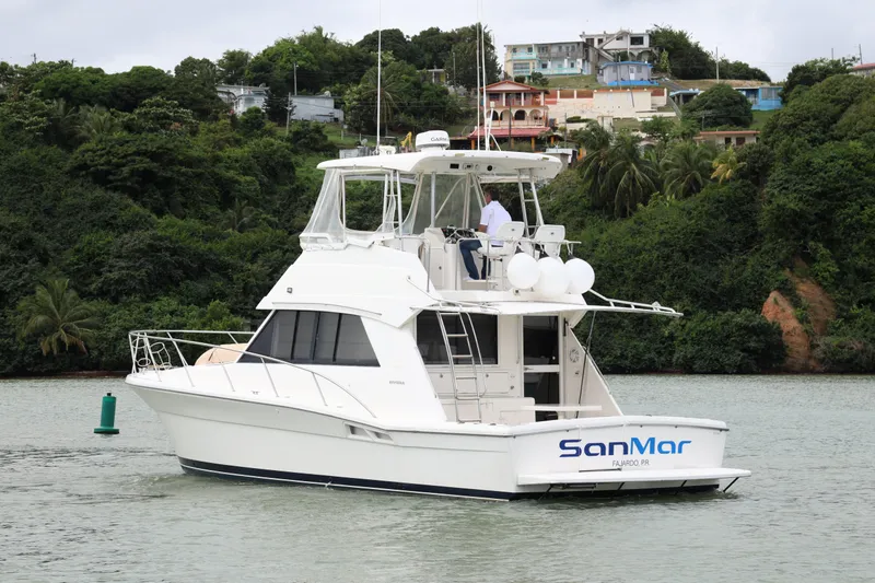 Slide: The Image of 2000 Riviera Flybridge Convertible yacht cruising near lush, green shoreline. - 6