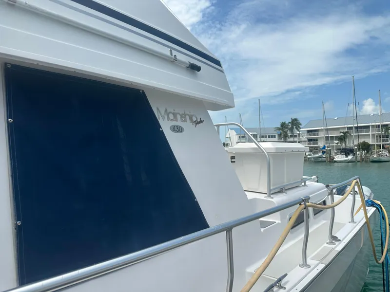 Slide: The Image of 1999 Mainship 430 Trawler docked at marina, blue canopy, clear sky background. - 26