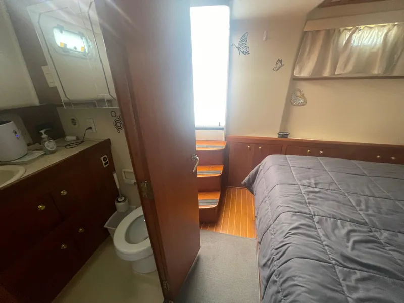 Slide: The Image of 1999 Mainship 430 Trawler interior with bedroom and bathroom, featuring wooden cabinetry and nautical decor. - 46
