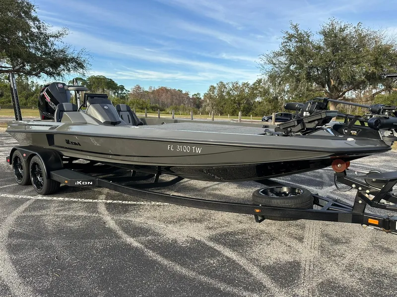 Slide: The Image of 2024 iKon LX21 boat on trailer in parking lot, surrounded by trees. - 0