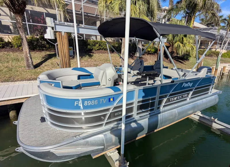 Slide: The Image of 2024 Trifecta 22TRFC LE 2.75 pontoon boat docked by palm trees. - 1