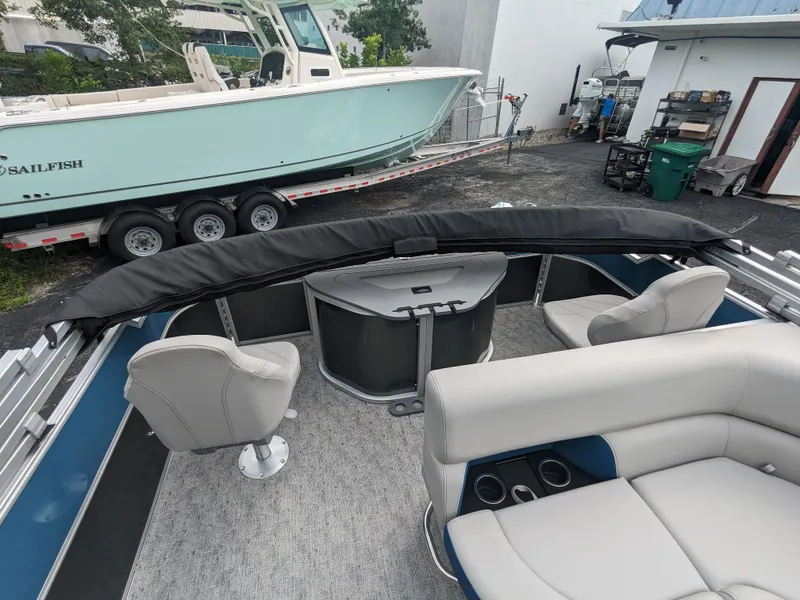 Slide: The Image of 2024 Trifecta 22TRFC LE 2.75 pontoon boat interior with seating and table, parked near another boat. - 26