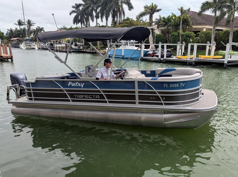 Slide: The Image of 2024 Trifecta 22TRFC LE 2.75 pontoon boat on water, featuring a canopy and sleek design. - 7