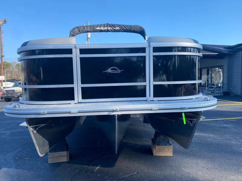 Slide: The Image of 2025 SunCatcher Select 322RC pontoon boat on display, black exterior, parked on wooden blocks. - 2