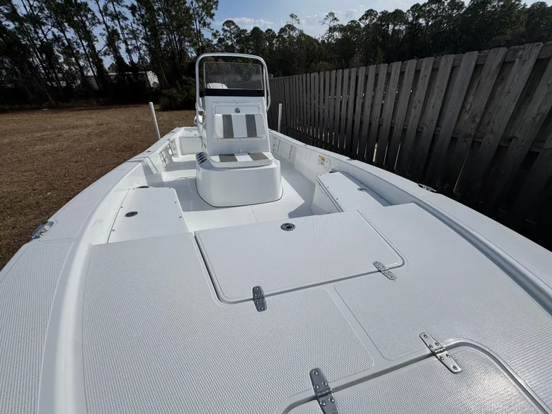 Slide: The Image of 2025 BlackJack 224 boat with spacious deck and seating, parked outdoors near a wooden fence. - 6