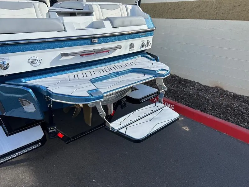 Slide: The Image of 2025 Malibu 23 MXZ boat rear view with swim platform and step, parked on pavement. - 10