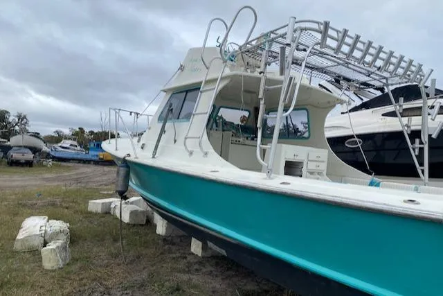 Slide: The Image of 1988 Robertson Sportfish boat on land, teal hull, overcast sky, marina background. - 2