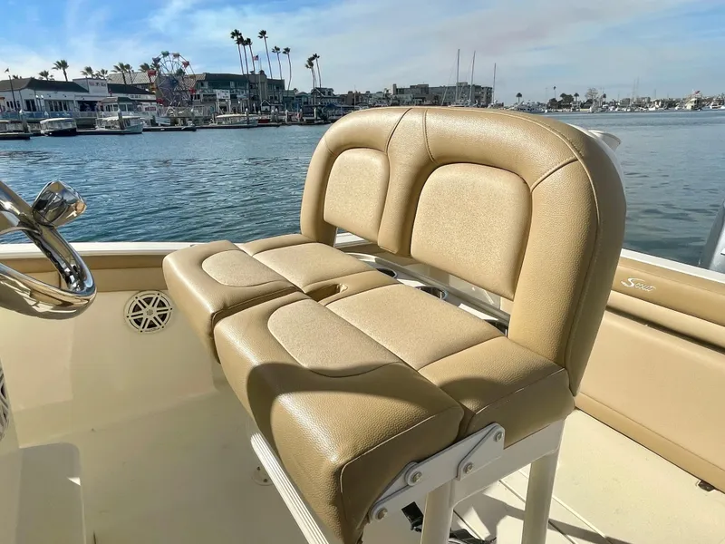 Slide: The Image of 2020 Scout 215 XSF boat with tan seating, docked by a scenic waterfront. - 23