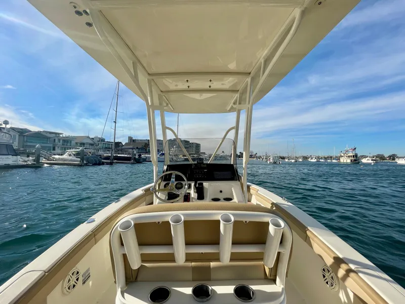 Slide: The Image of 2020 Scout 215 XSF boat on water, featuring helm and rod holders, under clear sky. - 34