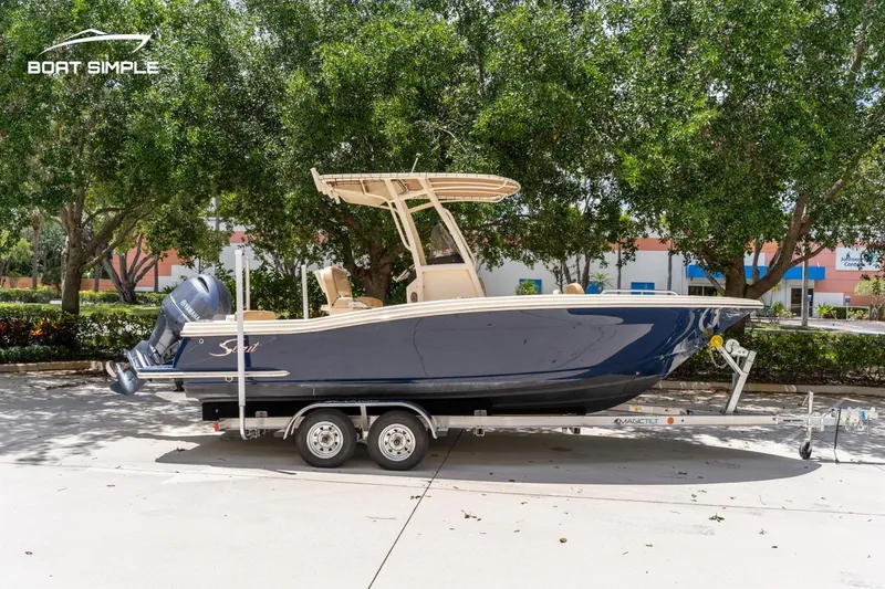 Slide: The Image of 2023 Scout 215 XSF boat on trailer, parked outdoors with trees in background. - 3