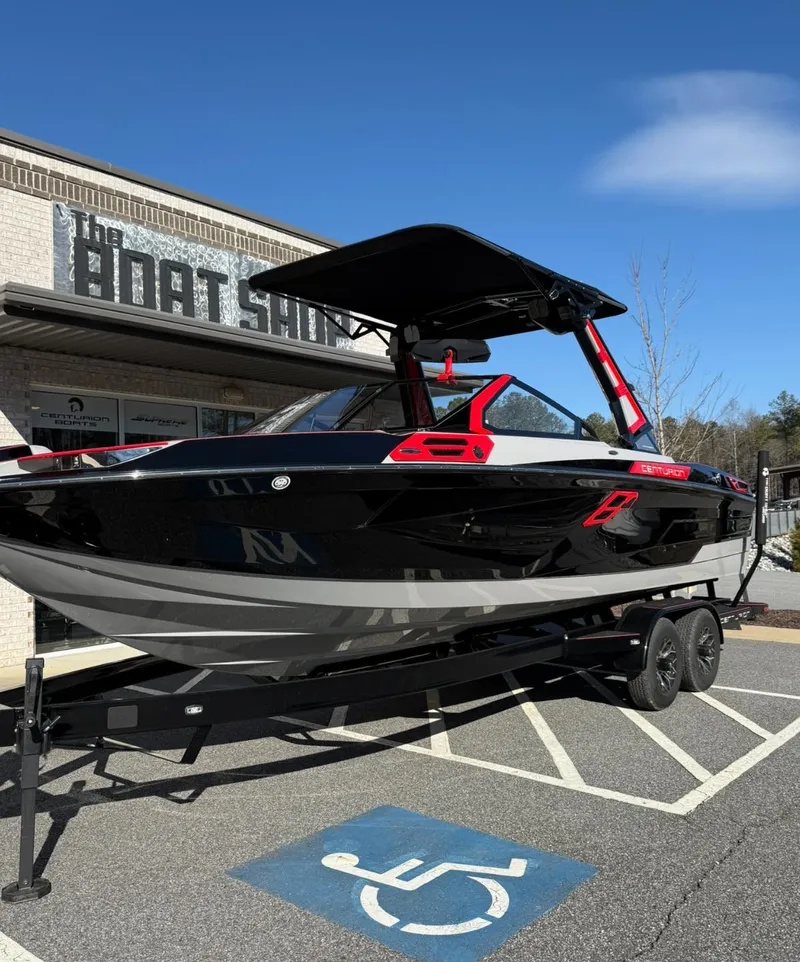 Slide: The Image of 2025 Centurion Ri245 boat on trailer outside dealership, featuring sleek black and red design. - 1