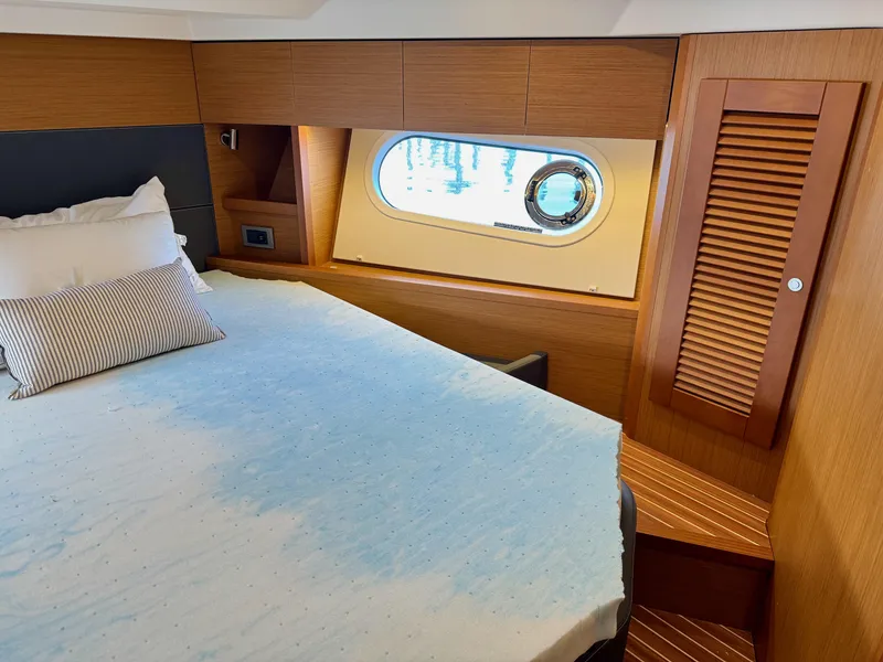 Slide: The Image of 2020 Beneteau Swift Trawler 47 cabin with bed, window, and wooden interior. - 23