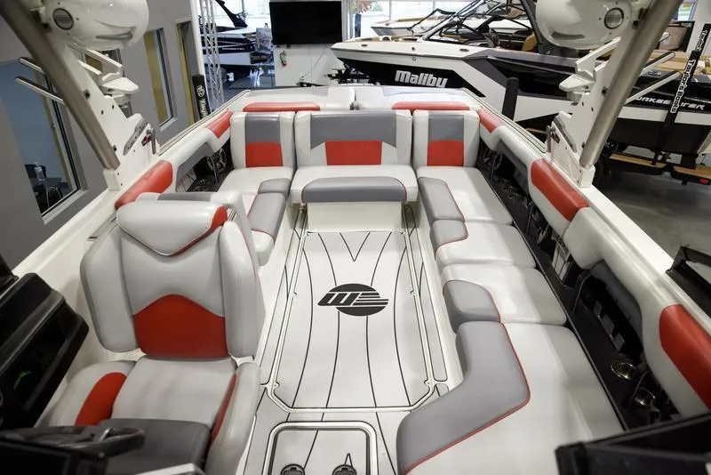 Slide: The Image of 2021 Malibu 25 LSV boat interior with red and gray seating in showroom. - 18