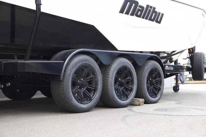 Slide: The Image of 2025 Malibu 25 LSV boat trailer with black wheels on pavement. - 7
