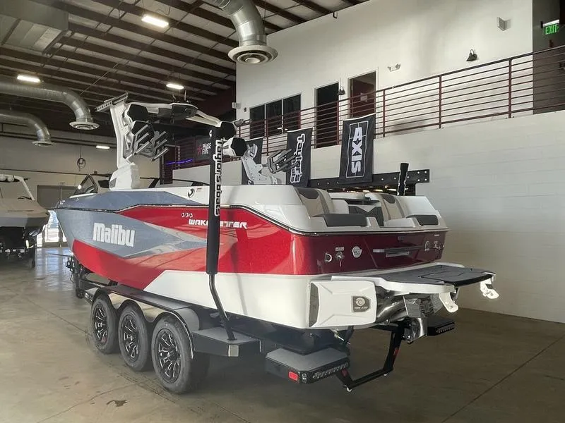 Slide: The Image of 2025 Malibu 25 LSV boat in showroom, red and white design, triple-axle trailer. - 10