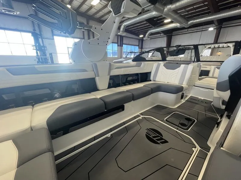 Slide: The Image of 2025 Malibu 25 LSV boat interior with sleek seating and modern design in a spacious warehouse. - 11