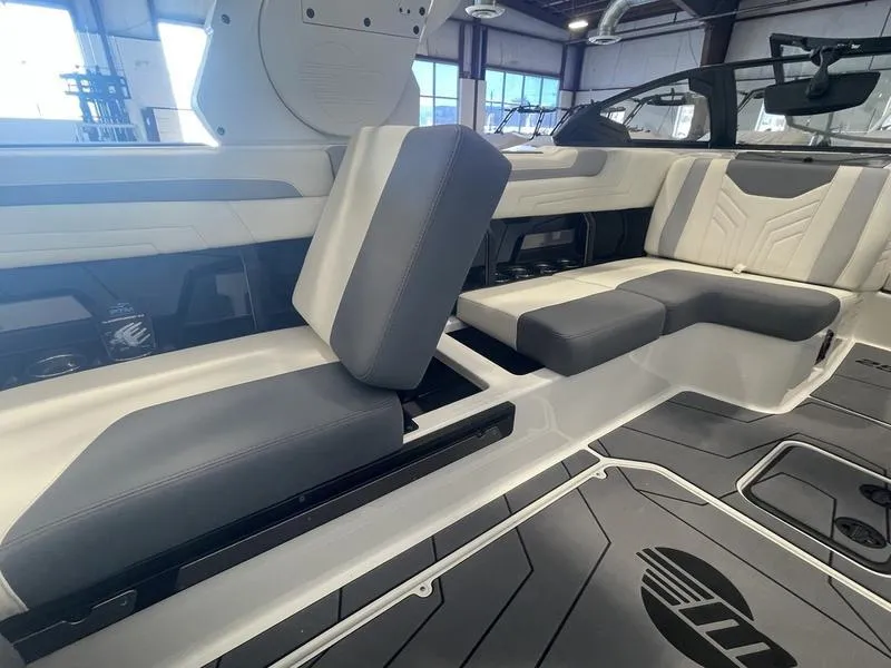 Slide: The Image of 2025 Malibu 25 LSV boat interior with gray and white seating in a showroom. - 21