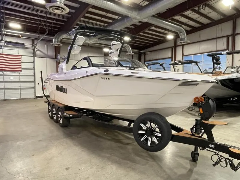 Slide: The Image of 2025 Malibu 26 LSV boat in showroom, white exterior, on trailer, industrial setting. - 5