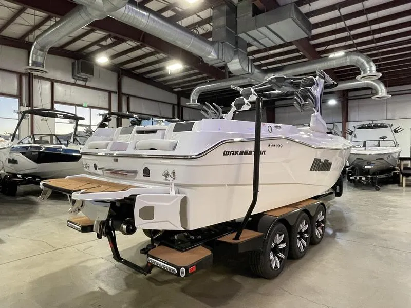 Slide: The Image of 2025 Malibu 26 LSV boat in a showroom, featuring a sleek design and triple-axle trailer. - 7