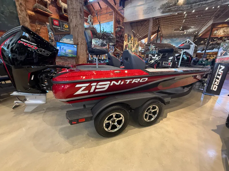 Slide: The Image of 2025 Nitro Z19 boat in showroom, red and black design, dual-axle trailer. - 2